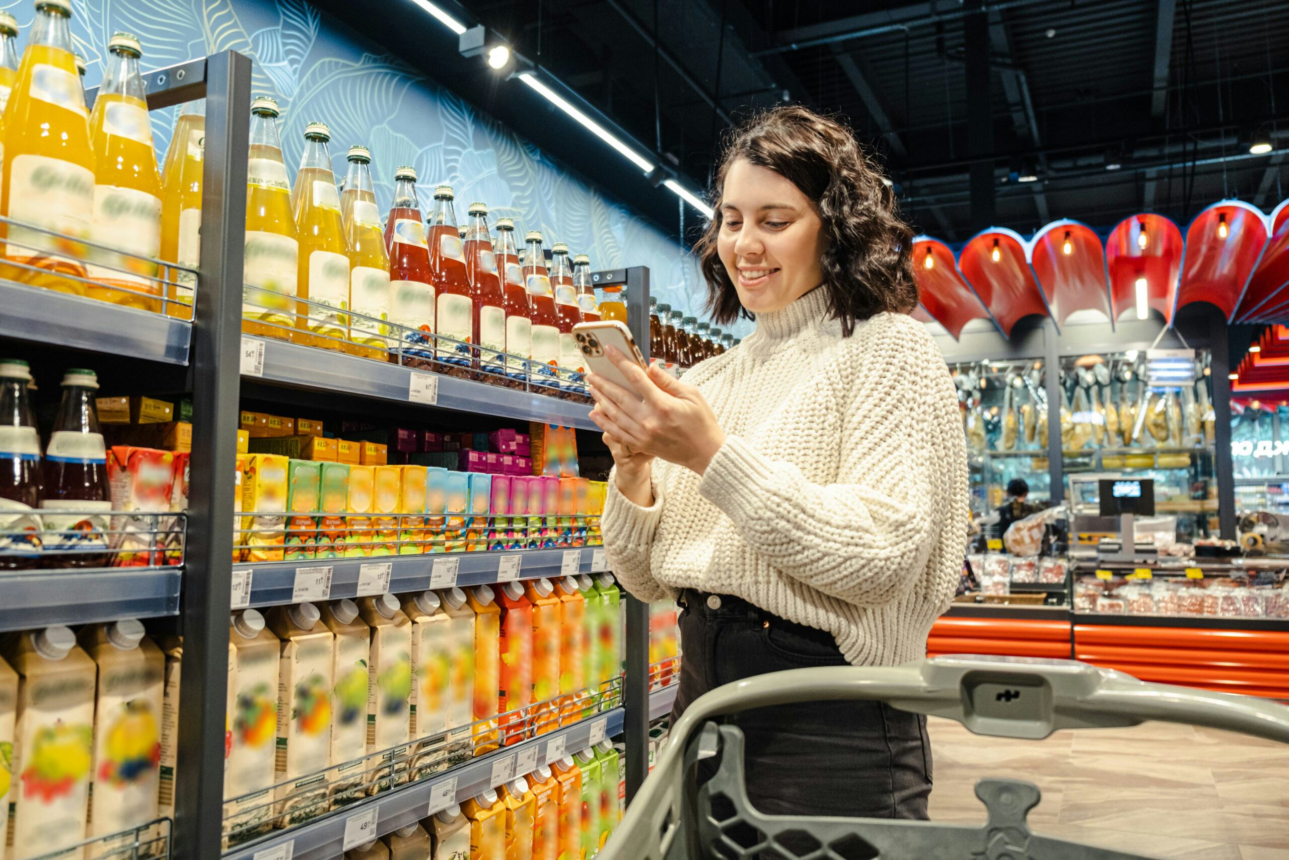 Woman shops juice using phone grocery list in supermarket